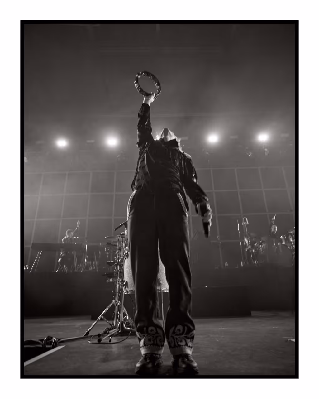 A stunning black and white film photo of a bands lead singer striking a pose on stage. Convert photo shot on film