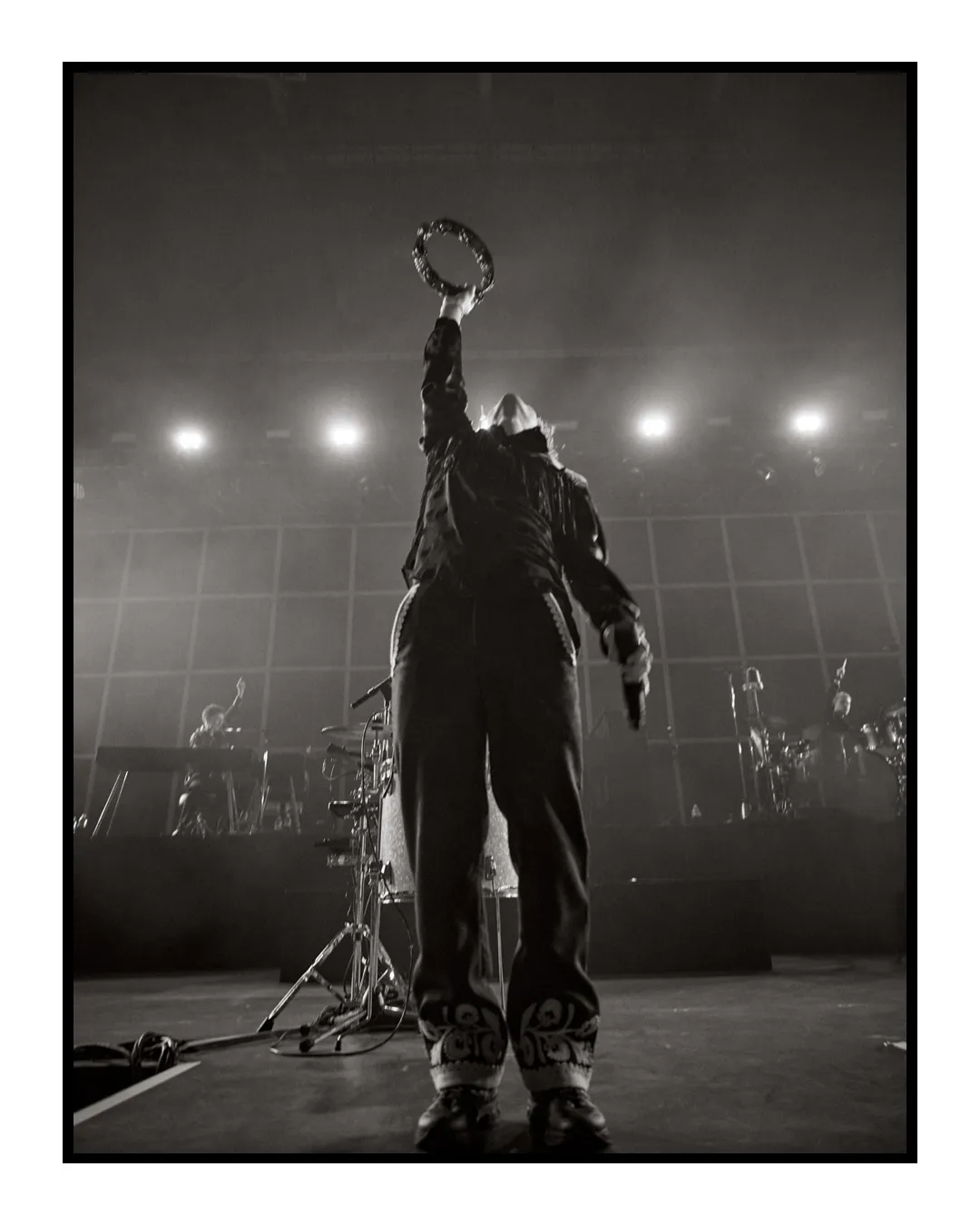 A stunning black and white film photo of a bands lead singer striking a pose on stage. Convert photo shot on film